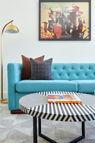 Midcentury modern living room with bright blue modern couch, round black and white coffee table, brass reading lamp.